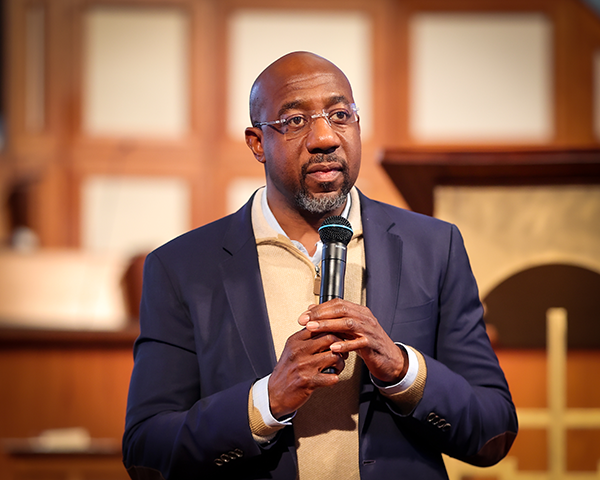 Rev. Raphael Warnock holding a microphone.